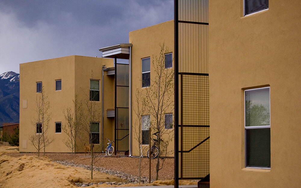Two-story ochre buildings at El Cerrito with young aspens, bikes by the doors, and a snow-capped peak behind
