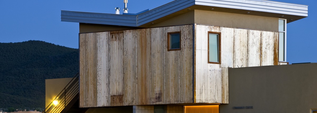 The weathered-steel community center at El Cerrito at dusk with forested foothills behind